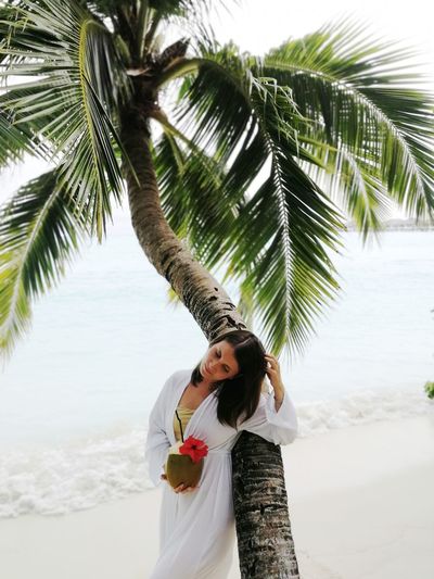 Woman standing by palm tree on beach