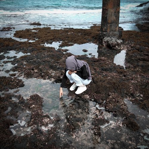 High angle view of woman crouching on rock by sea