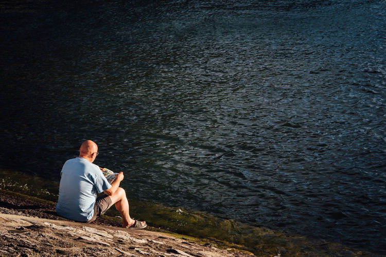 Rear view of man sitting by lake