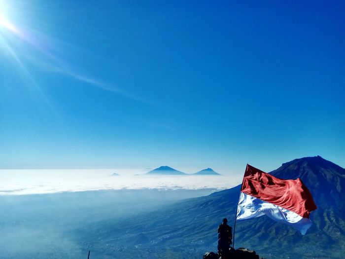 Rear view of people with indonesian flag on mountain against clear blue sky