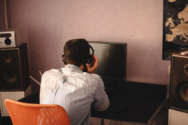 Man holding headphones while listening music sitting by computer