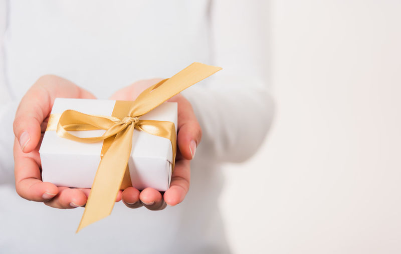 Cropped hand of woman holding gift against white background