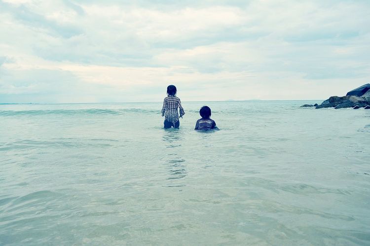Rear view of children in sea against sky
