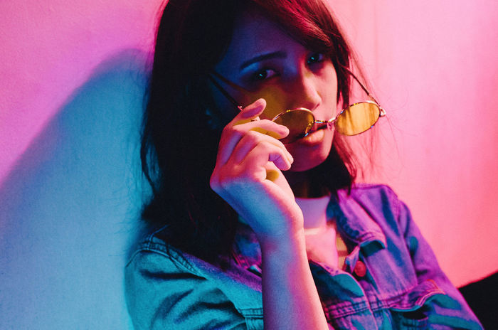 Portrait of young woman holding sunglasses against wall at nightclub