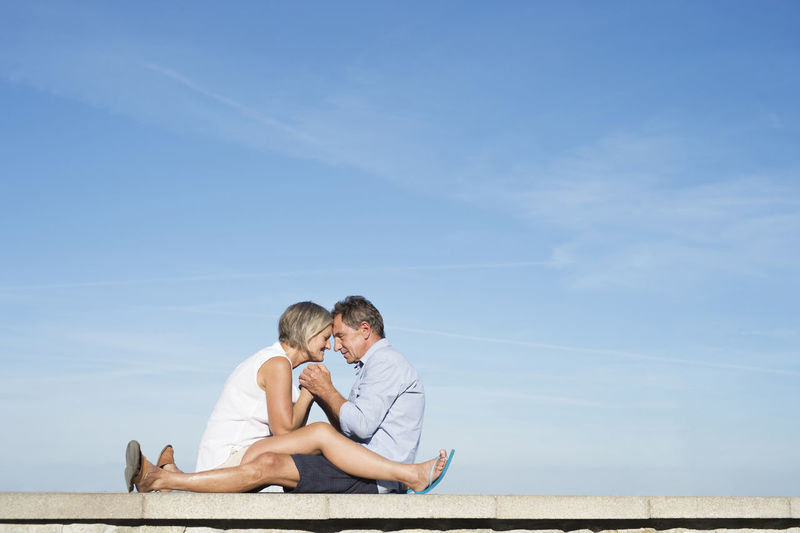 Senior couple sitting head to head on a wall in front of the city