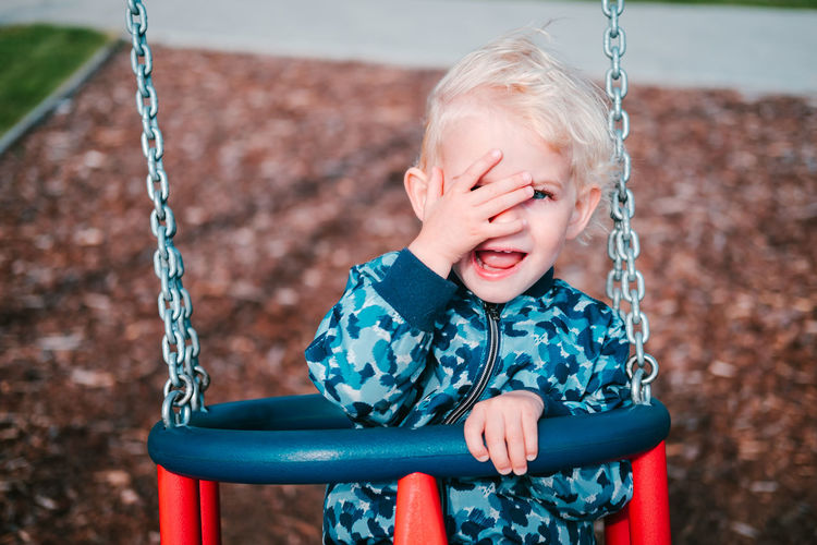 Young toddler boy swinging at children playground.