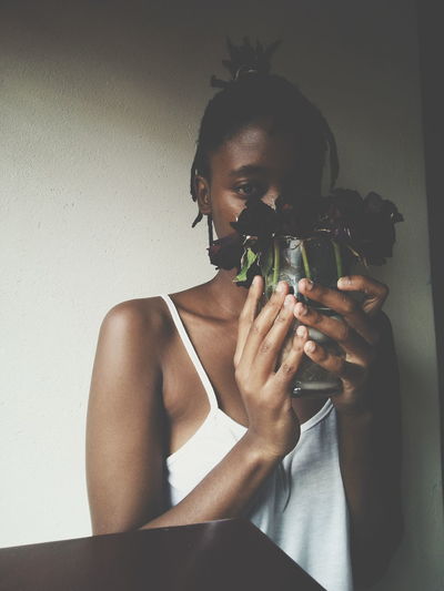 Close-up portrait of woman holding flowers against wall at home
