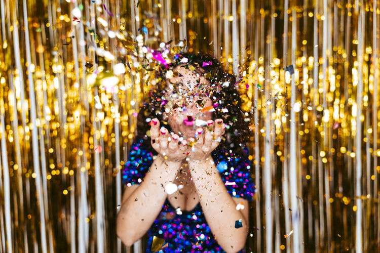 Portrait of woman blowing confetti against tinsel