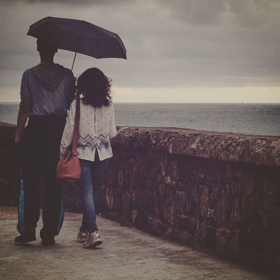 Rear view of man and woman walking under umbrella on walkway