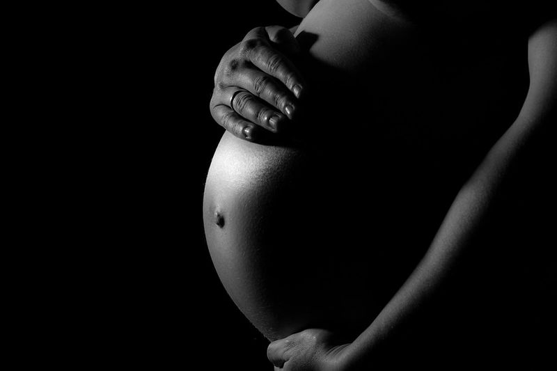 Midsection of pregnant woman touching belly against black background