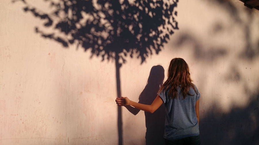 Optical illusion on woman holding tree shadow on wall