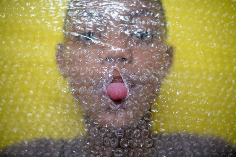 High angle view portrait of boy sticking out tongue through bubble wrap