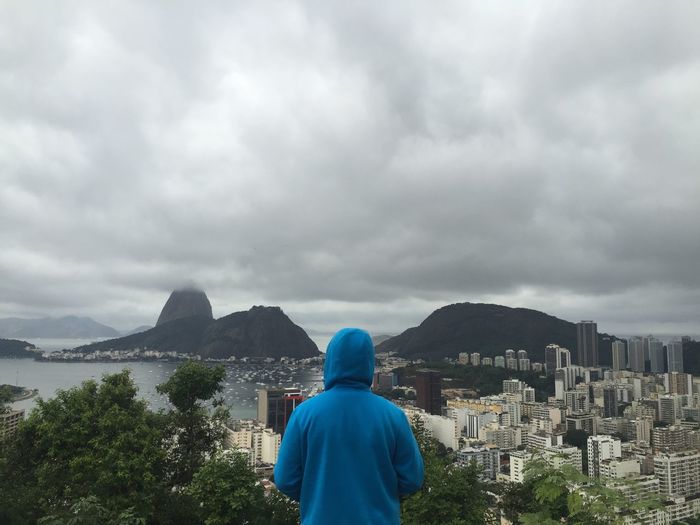 Rear view of man looking at cityscape against cloudy sky