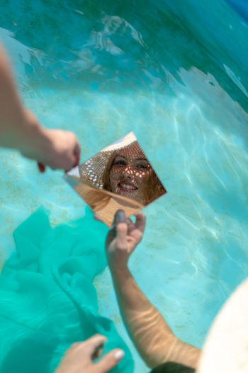 Cropped hand and young woman holding mirror with reflection in wading pool