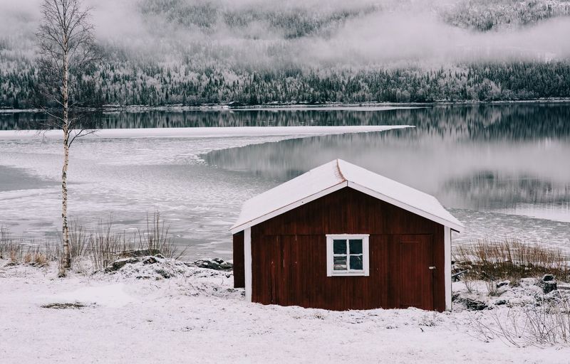 Snow covered cottage by lake