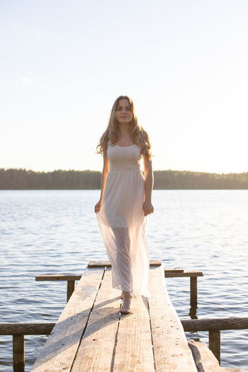 Portrait of young woman standing by lake against clear sky