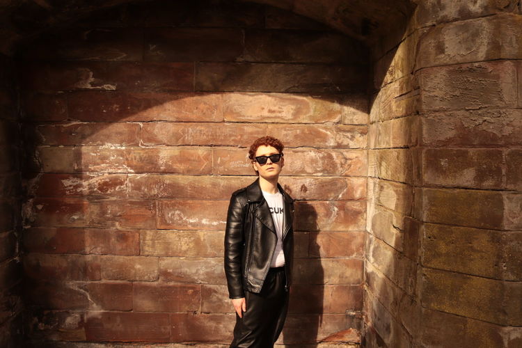 Portrait of young man standing against brick wall