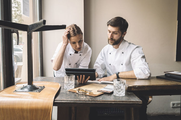 Chef with coworker looking at digital tablet at table in restaurant