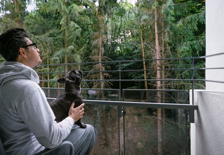 Man with dog sitting in balcony against trees