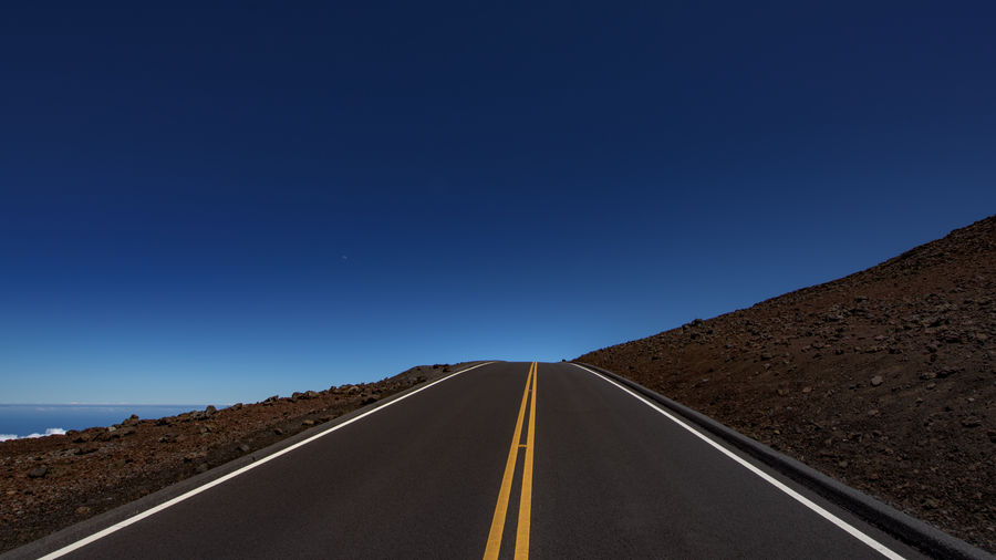 Road passing through landscape against clear blue sky