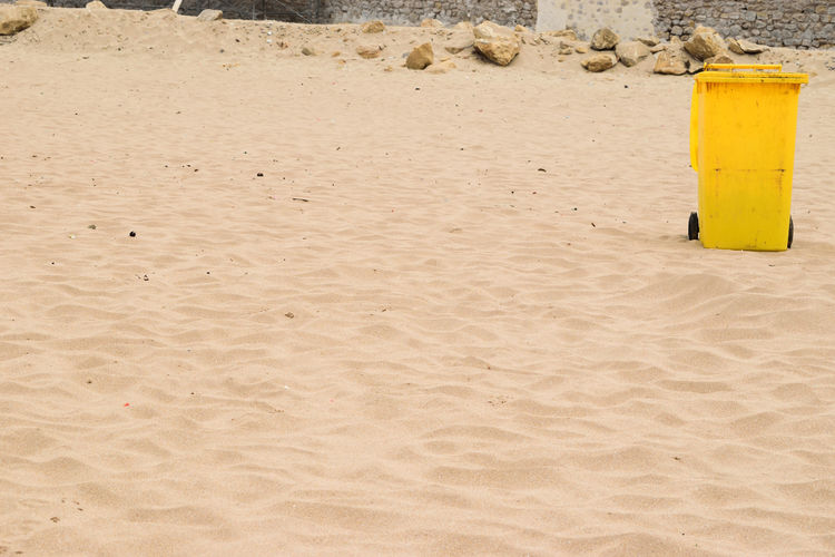 Yellow garbage container and trash in a sandy and clear beach in summer 
