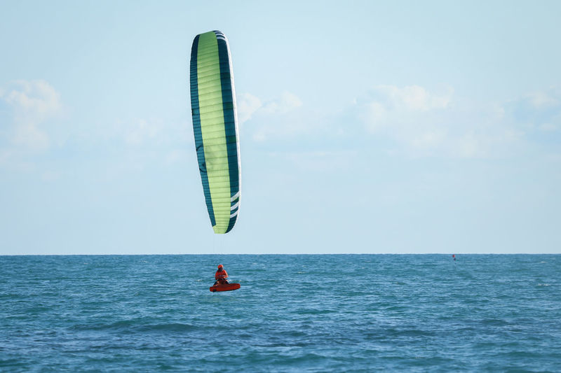 Person paragliding in sea against sky