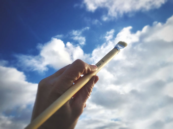 Low angle view of hand holding cigarette against sky
