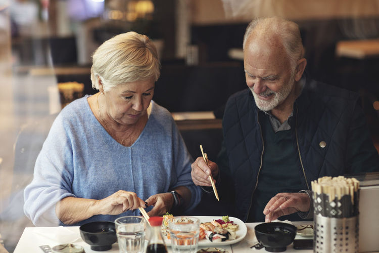Senior couple eating food while sitting in restaurant