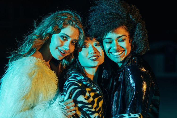 Portrait of smiling young women while standing outdoors at night