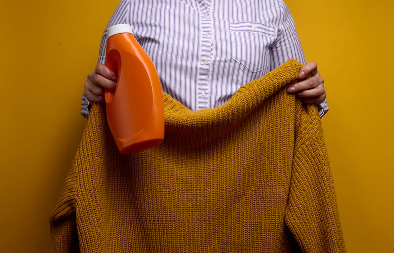 A woman in a white striped shirt holds an orange plastic bottle with liquid washing gel and a 