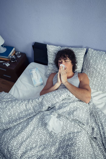 High angle view of young man with flu on bed at home
