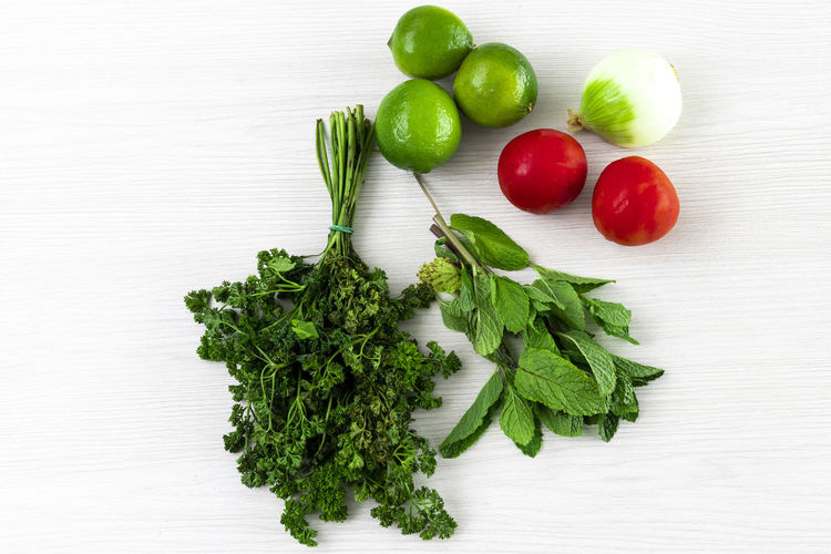 Bundles and mint packets with lemons, tomatoes and onion on white wooden textured background