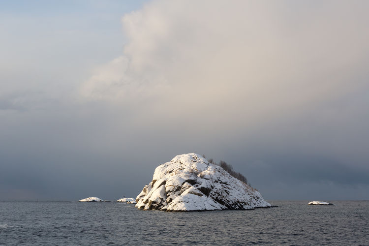Snow covered rock formation in sea against cloudy sky