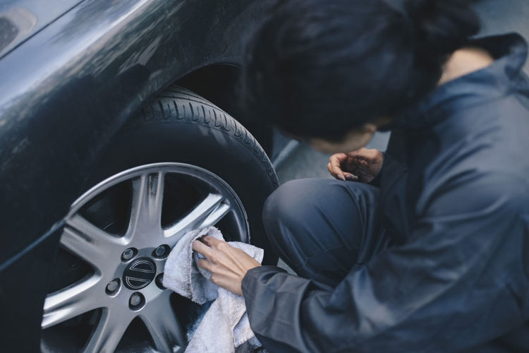 Female mechanic cleaning car wheel rim outside auto repair shop