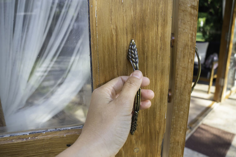 Close-up of hand holding wooden door