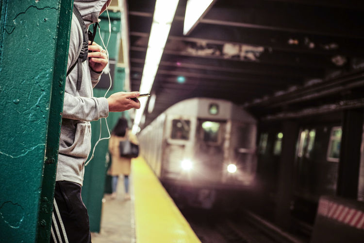 Midsection of man listening music while standing by train at railroad station platform