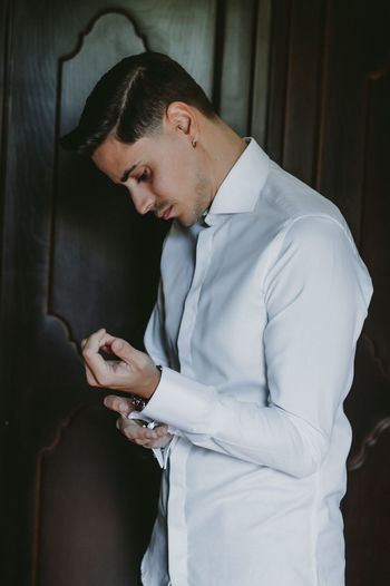 Side view of groom getting dressed