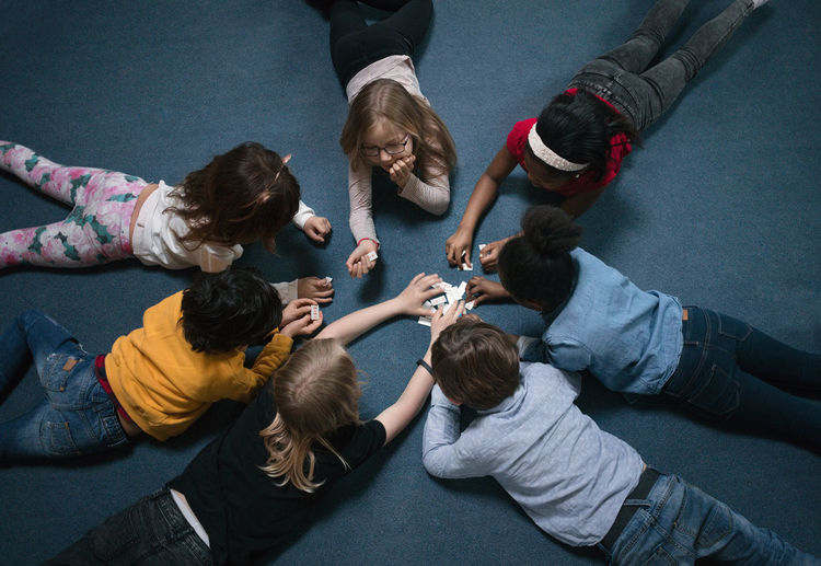 Directly above shot of children playing while lying on floor in school