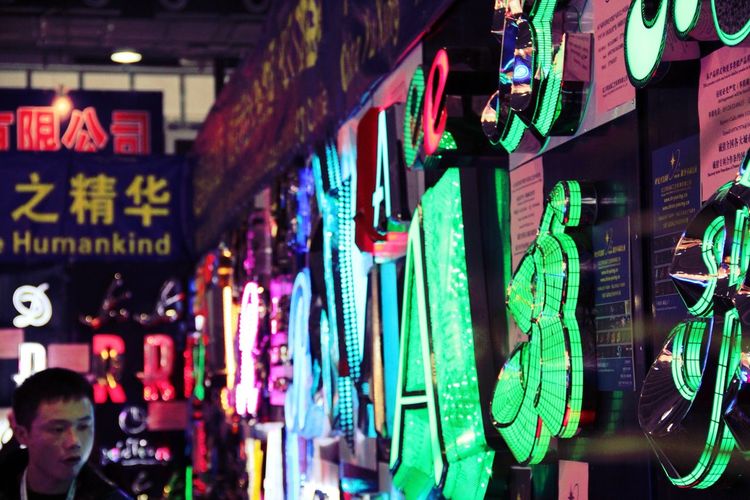 Man by illuminated neon signs at market