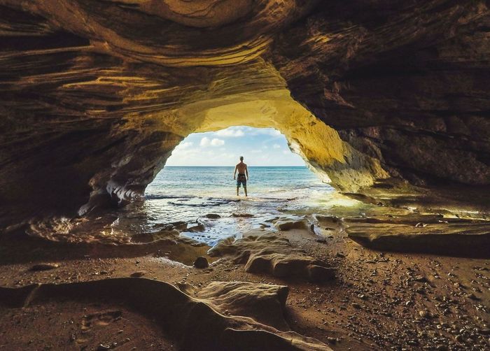 Rear view of man standing against sea seen through cave