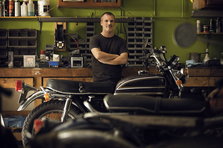 Portrait of confident owner standing by motorcycle in workshop