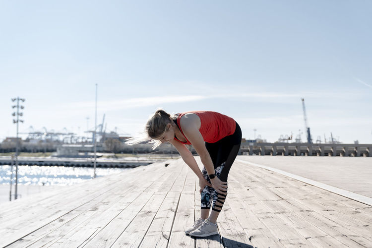 Young female athlete resting on pier during sunny day