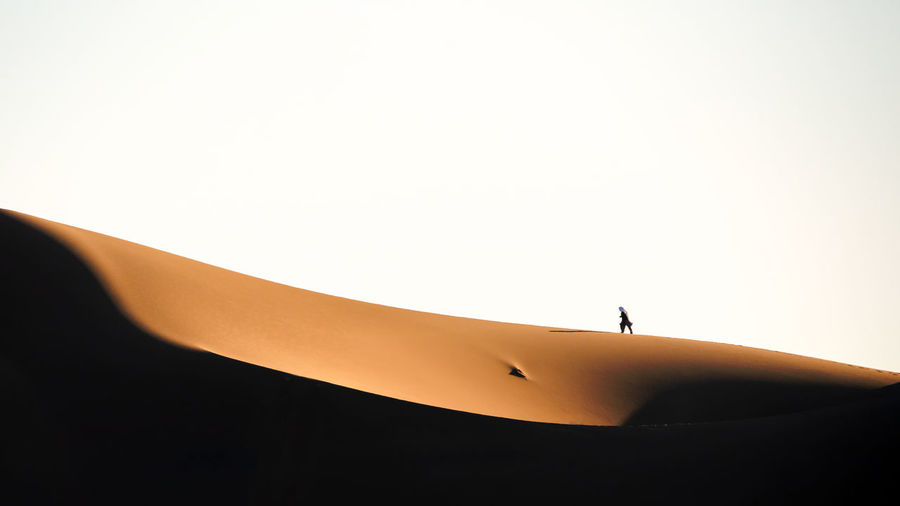 Silhouette person on sand dune against clear sky
