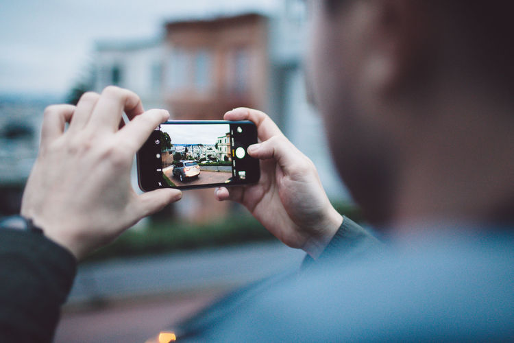 Cropped image of man photographing car through mobile phone