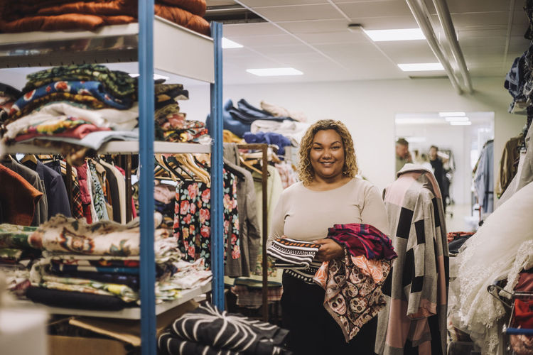Portrait of smiling female fashion designer holding fabrics while standing at workshop