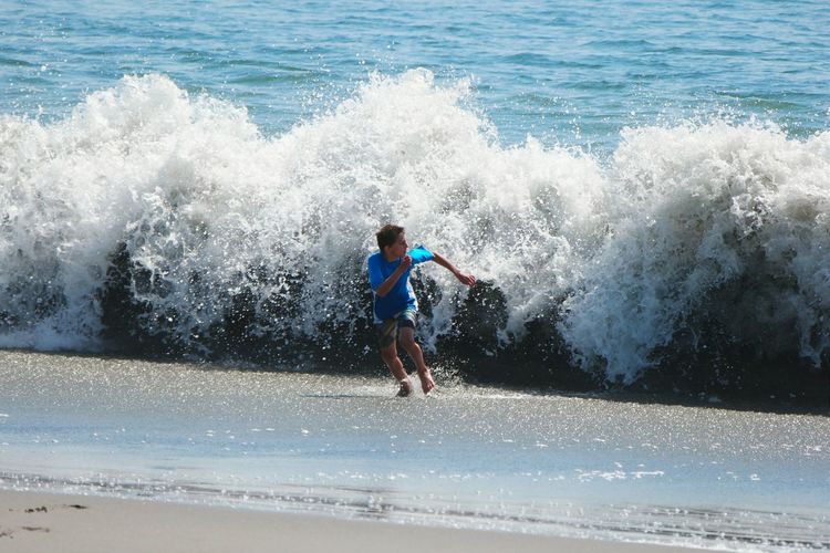 Teenage boy running against waves at beach