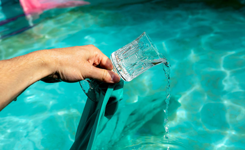 Cropped hand of men pouring drinking water in swimming pool