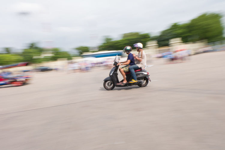 Men riding motor scooter on street