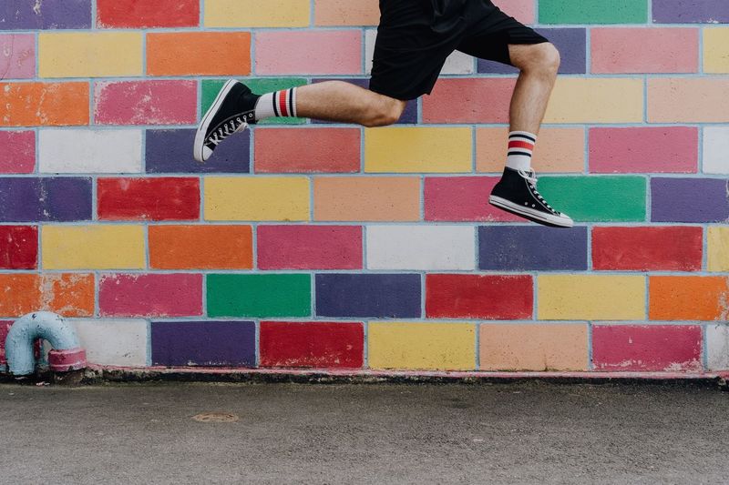 Low section of man jumping against colorful wall