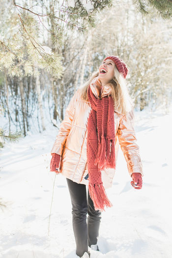 Happy young woman enjoying by trees on snowy field in winter